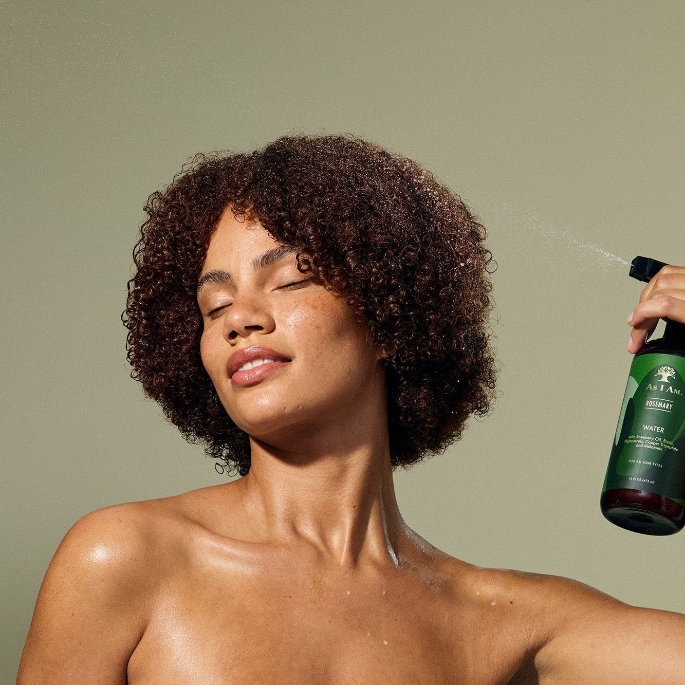 Vrouw met natuurlijk krullend haar die As I Am Rosemary Water spray gebruikt voor hydratatie en verzorging