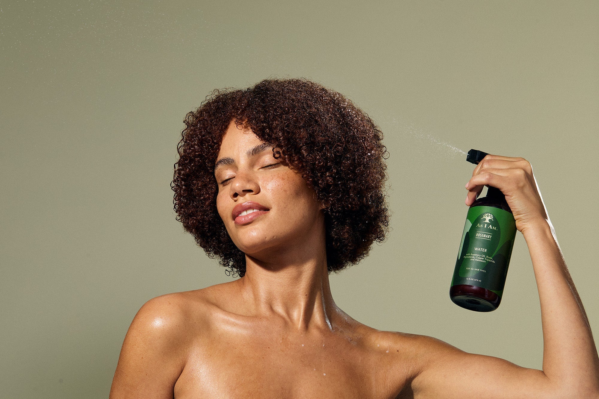Vrouw met natuurlijk krullend haar die As I Am Rosemary Water spray gebruikt voor hydratatie en verzorging
