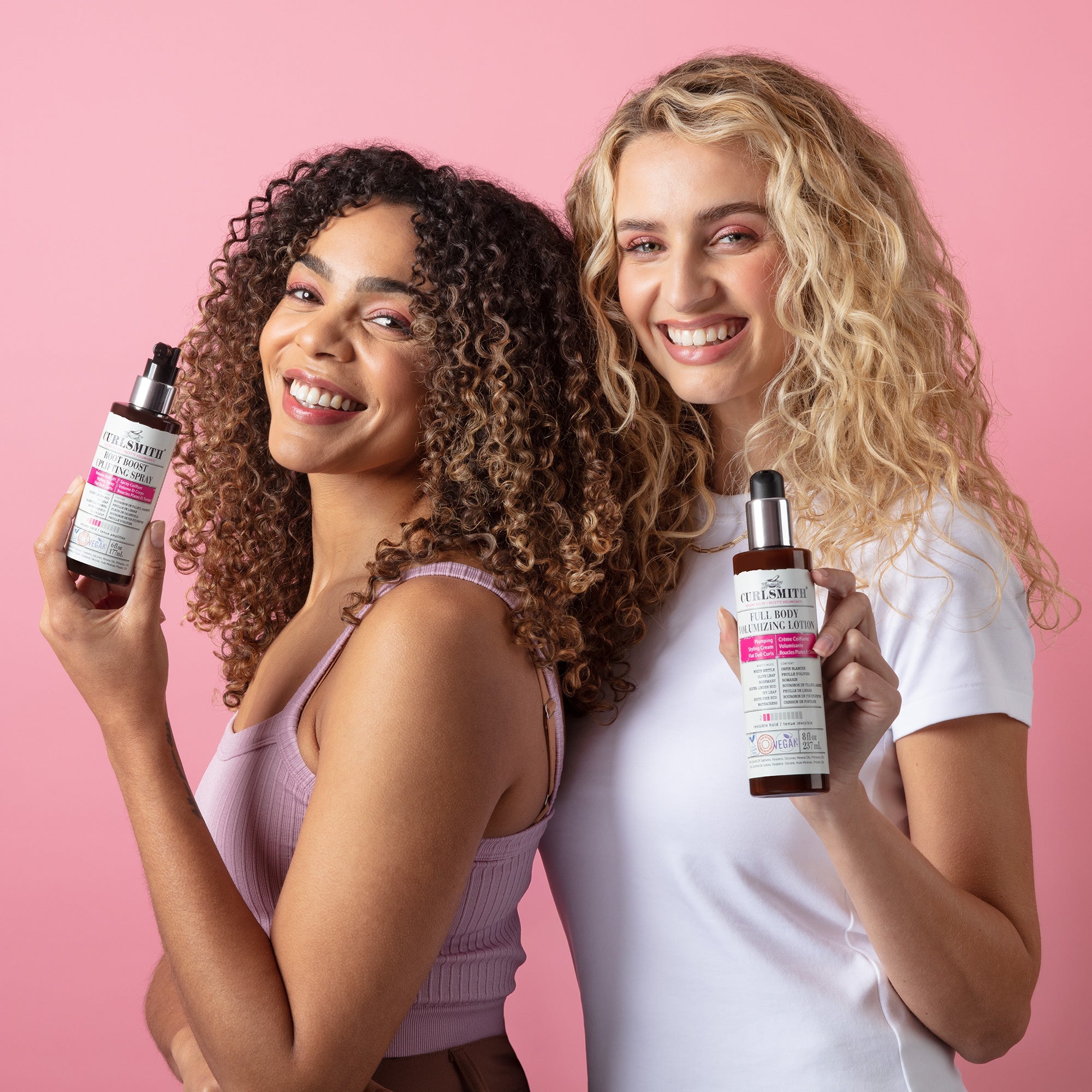 Twee vrouwen met krullend haar houden Curlsmith haarproducten vast – natuurlijke verzorging voor glanzende, gezonde krullen. Verkrijgbaar bij Beauty Source.