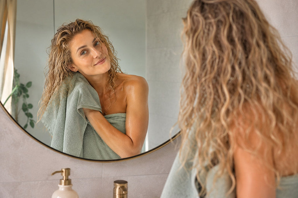 vrouw blonde krullen handdoek badkamer spiegel