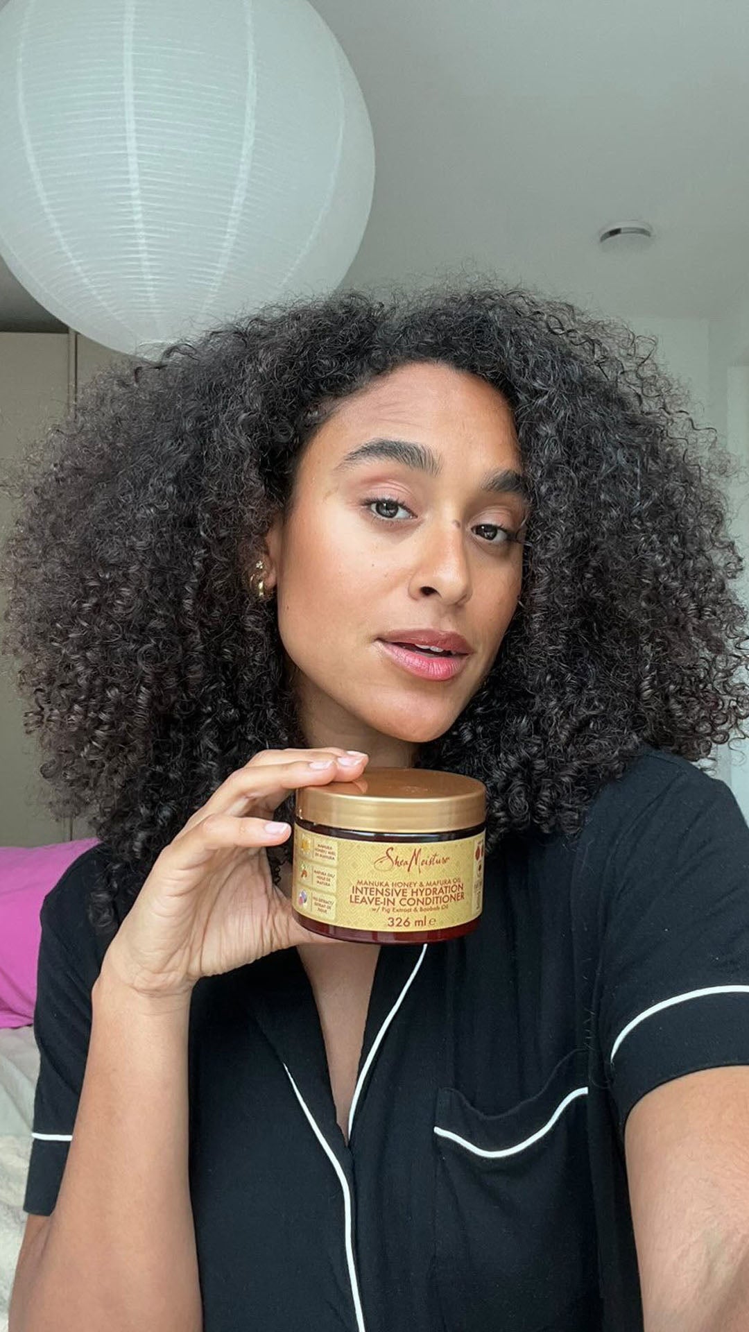 Coeshi van der Puye met natuurlijk krullend haar houdt SheaMoisture Intensive Hydration Leave-In Conditioner vast – hydraterende conditioner voor krullen online kopen bij Beauty Source.